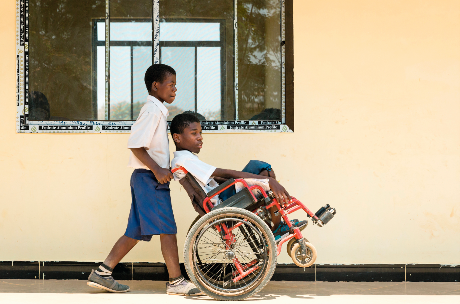 A boy pushing another boy in a wheelchair at a school in Tanzania. 